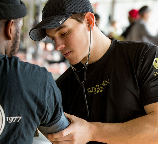 Kutztown University student taking another student's blood pressure using a cuff and stethoscope