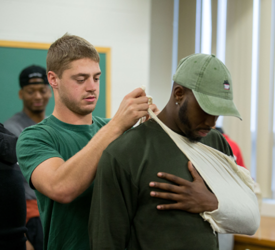 Kutztown University student putting a sling on the arm of another student